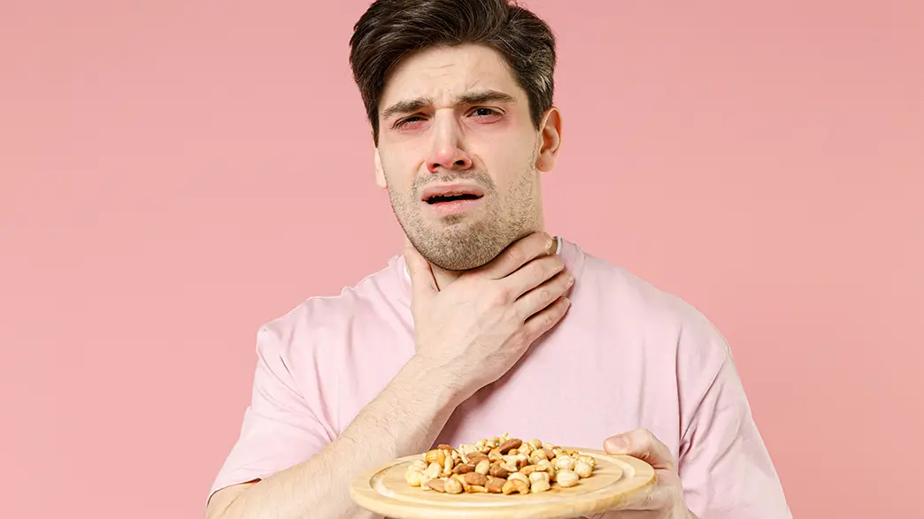 A man with a peanut allergy experiences allergic symptoms after eating some nuts with red eyes and 
                shortness of breath – he grasps his throat