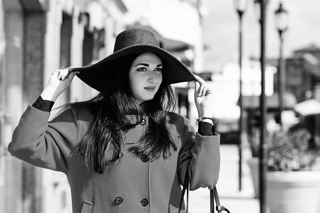 Confident young woman in a long red coat and wide-brimmed sun hat