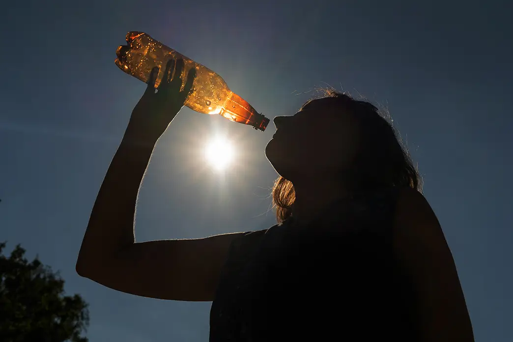 A woman drinks water from a bottle under the bright sun